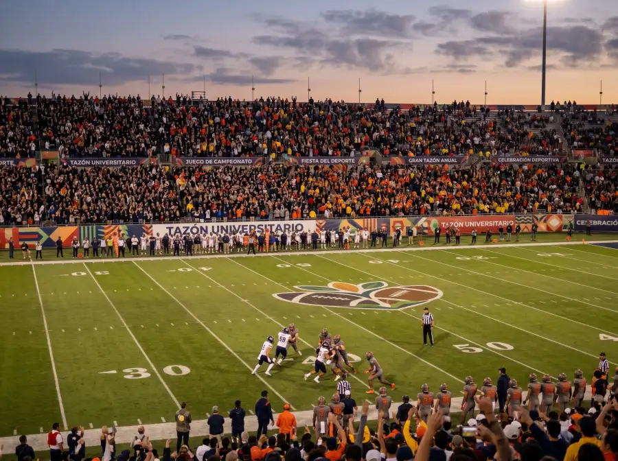 Estadio decorado para un bowl game universitario con gradas llenas al atardecer