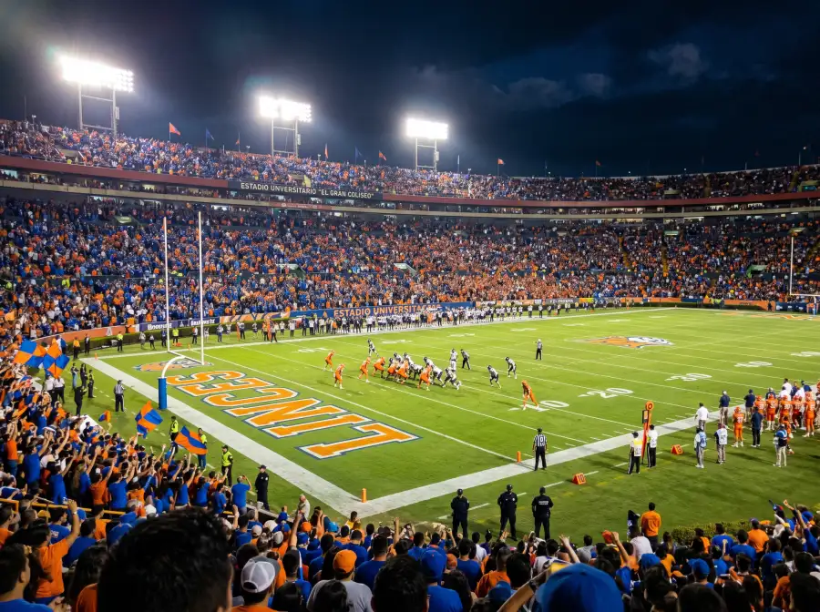 Estadio universitario de NCAA football lleno durante un partido nocturno con la afición local